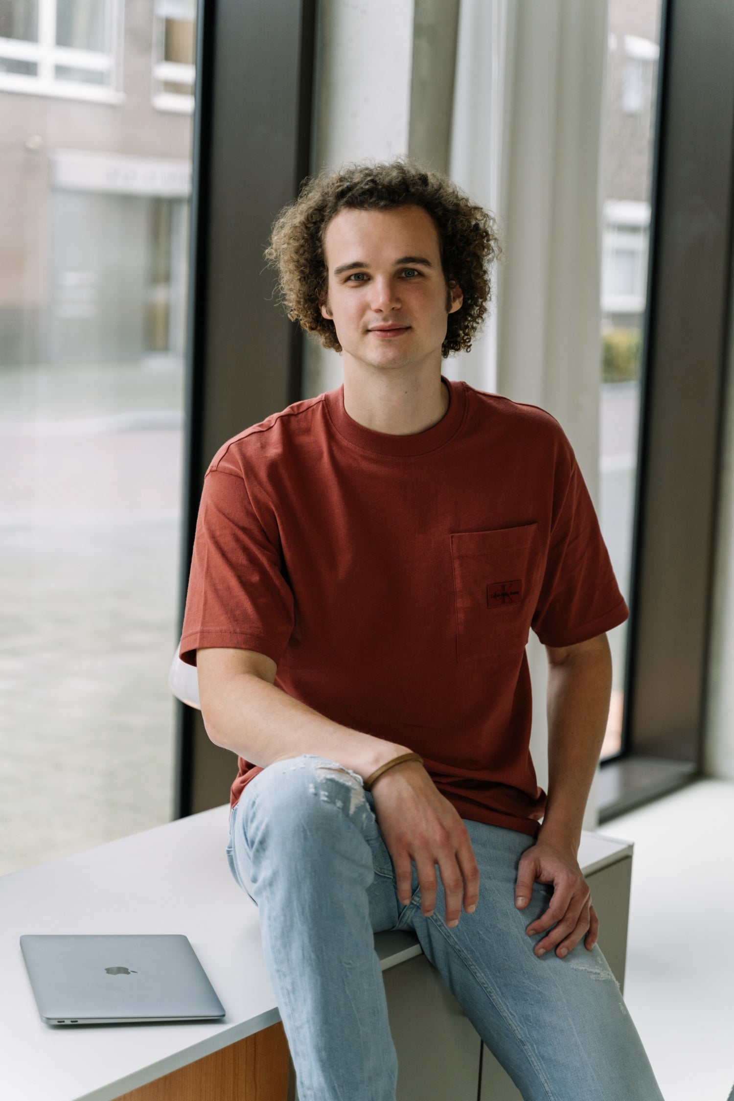 De WBshopmaker lachend naar de camera, zittend op een bureau