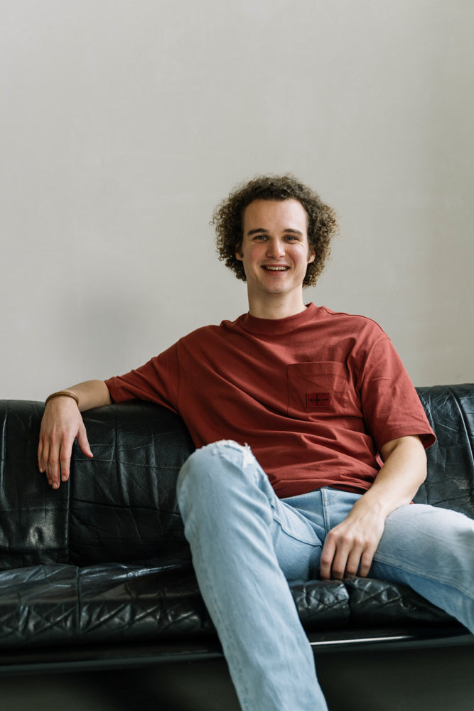 De WBshopmaker lachend naar de camera op een zwarte bank